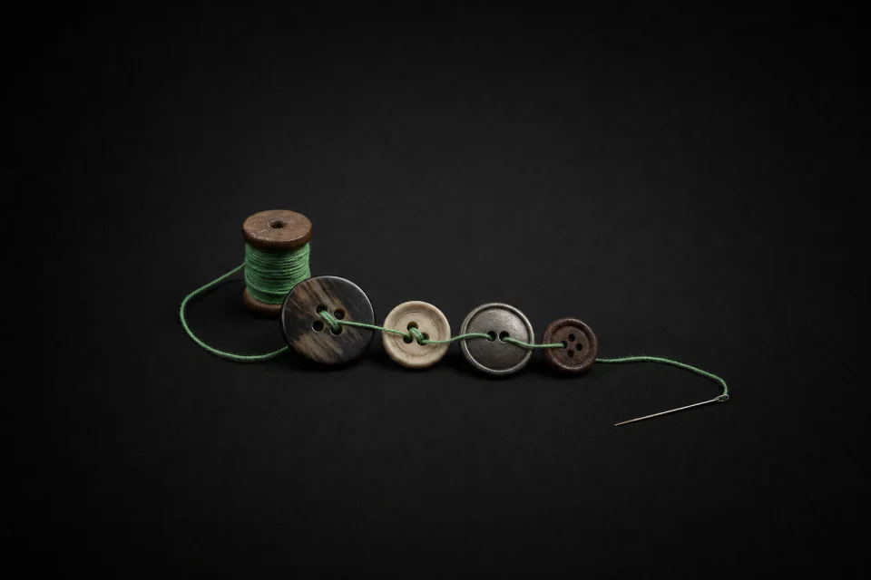 One thread stitched through four different buttons in order, from a spool to a needle
