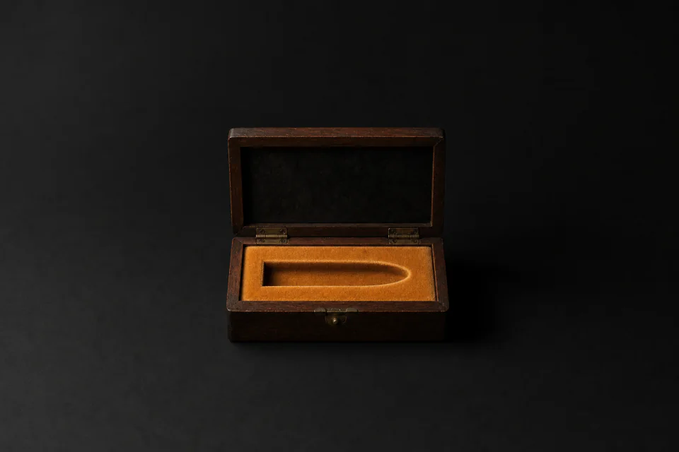 An open walnut case whose velvet lining is moulded for a single bullet, and the recess is empty