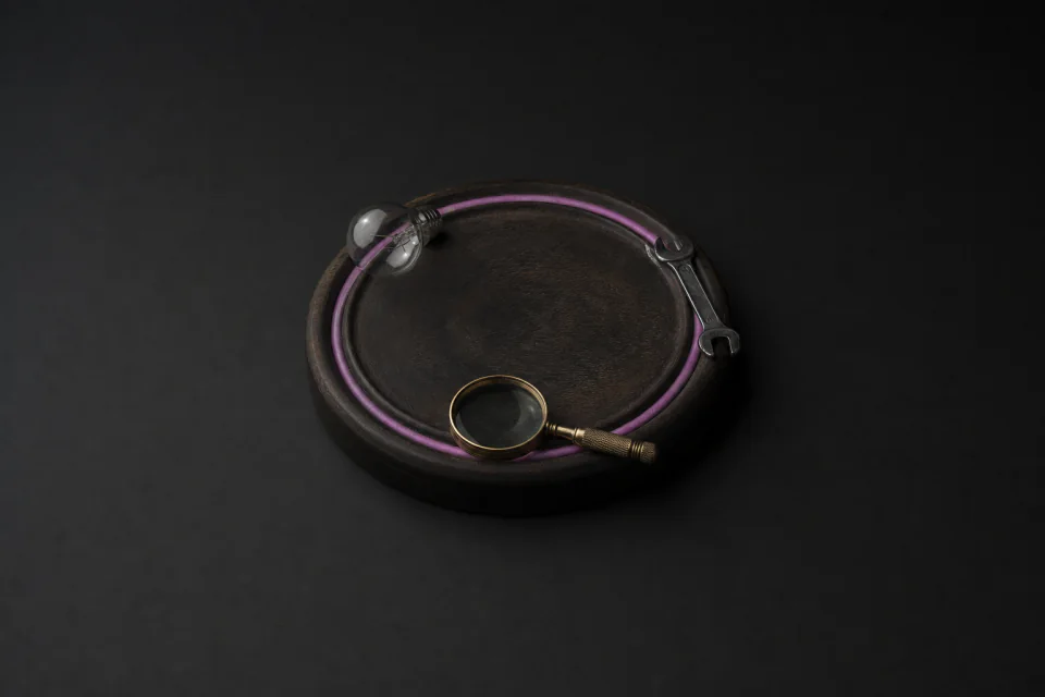 A round tray with a closed groove carrying a lightbulb, a wrench and a magnifying glass around the loop